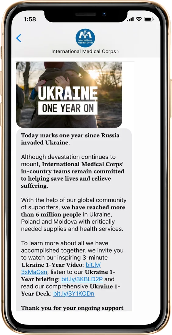 Text message from International Medical Corps marking one year since Russia's invasion of Ukraine, with an image of two people embracing at sunset and a note that more than 6 million people have been reached.